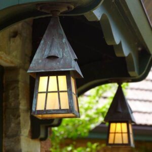 Verdigris ceiling lantern with glowing gold glass beneath a green wooden bracket, with a second lantern behind it.